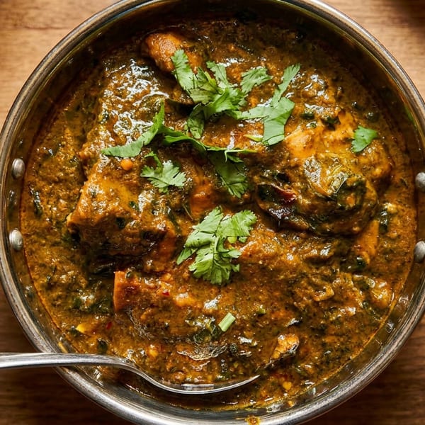 Rich Indian chicken curry with cilantro in a brass karahi, with a spoon on a wooden table.