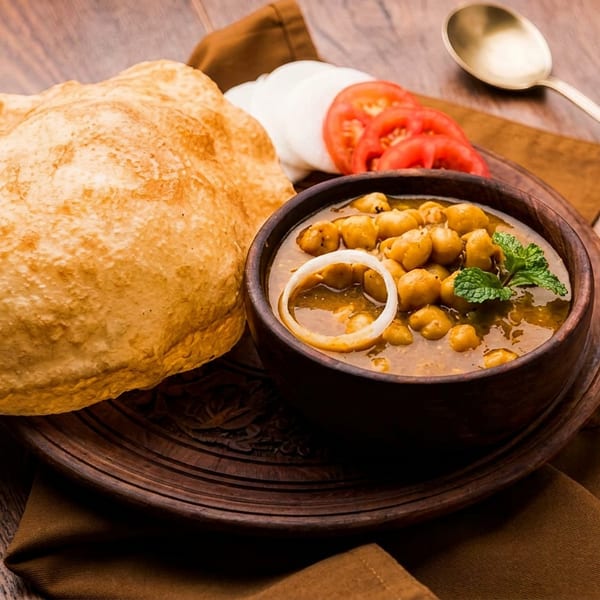 Chole bhature with sliced onions, tomatoes, and mint on a wooden table.