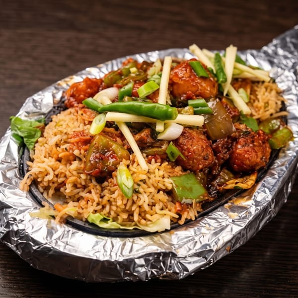 Spiced fried rice topped with saucy vegetables, meatballs, peppers, and scallions in a foil-lined serving dish.