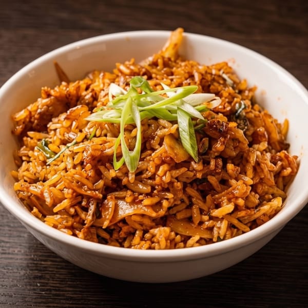 Bowl of richly spiced fried rice topped with sliced green onions on a dark wooden table.