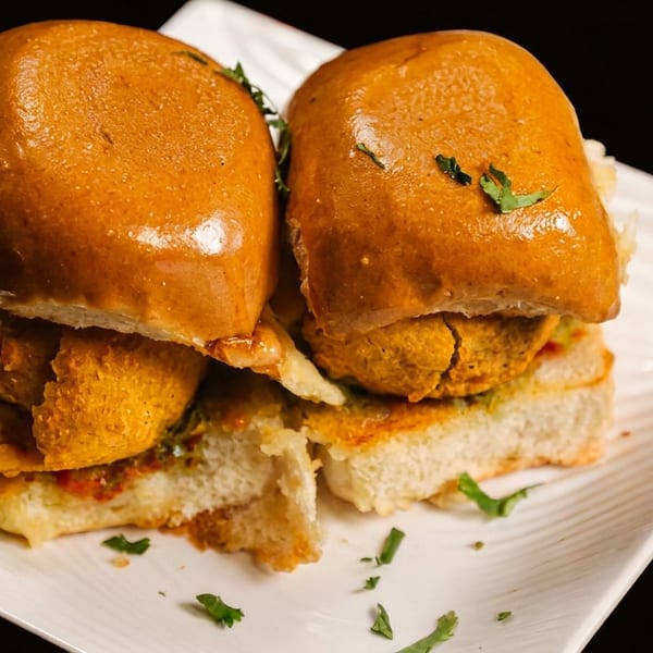 Two Indian vada pav sandwiches with fried potato patties and cilantro on a white plate.
