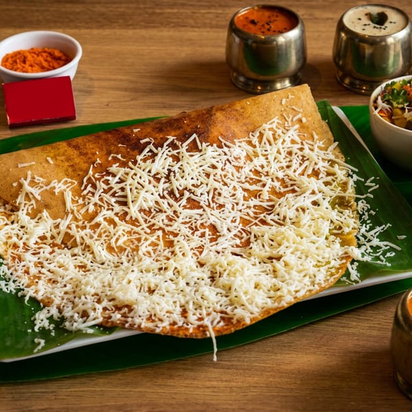 Cheese dosa on a banana leaf, served with sambar, chutneys, and a vegetable side dish.