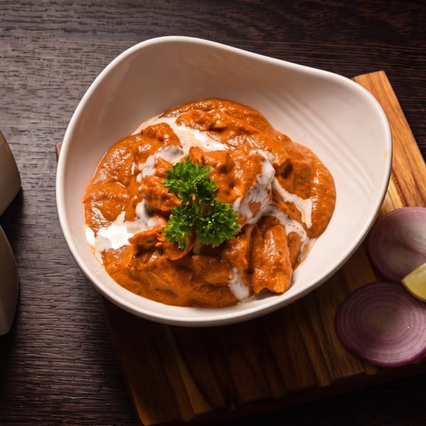 Creamy orange curry garnished with parsley in a white bowl, served with sliced red onion and lime on a wooden board.