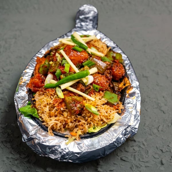 Chili chicken and fried rice served on a foil-wrapped sizzling platter, garnished with ginger and green onions.